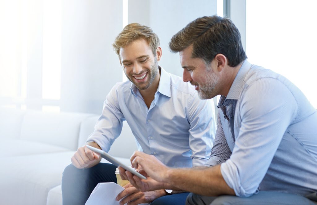 young and mature businessmen smiling while using a digital table