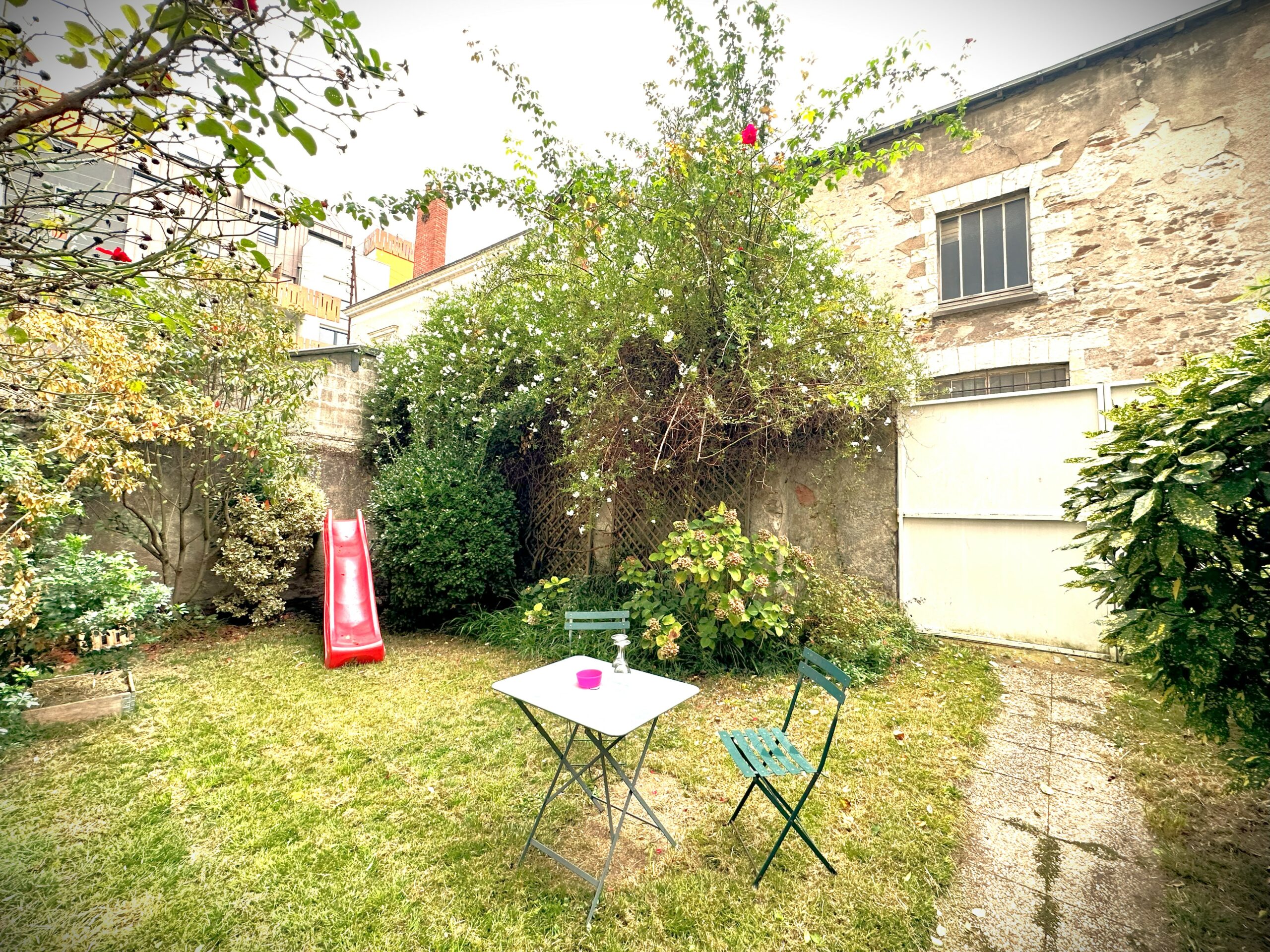 Jardin paysager avec petite table et deux chaises. Toboggan pour enfant en fond