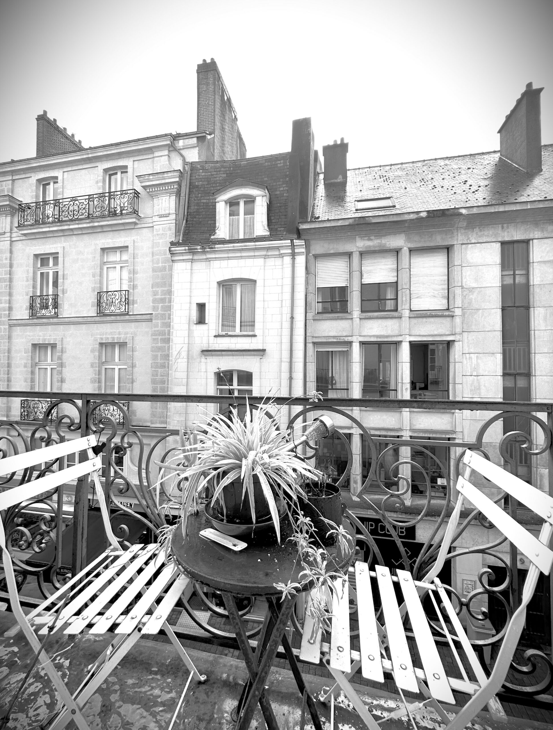 Balcon avec table et chaises, immeuble ancien en fond. Image noir et blanc