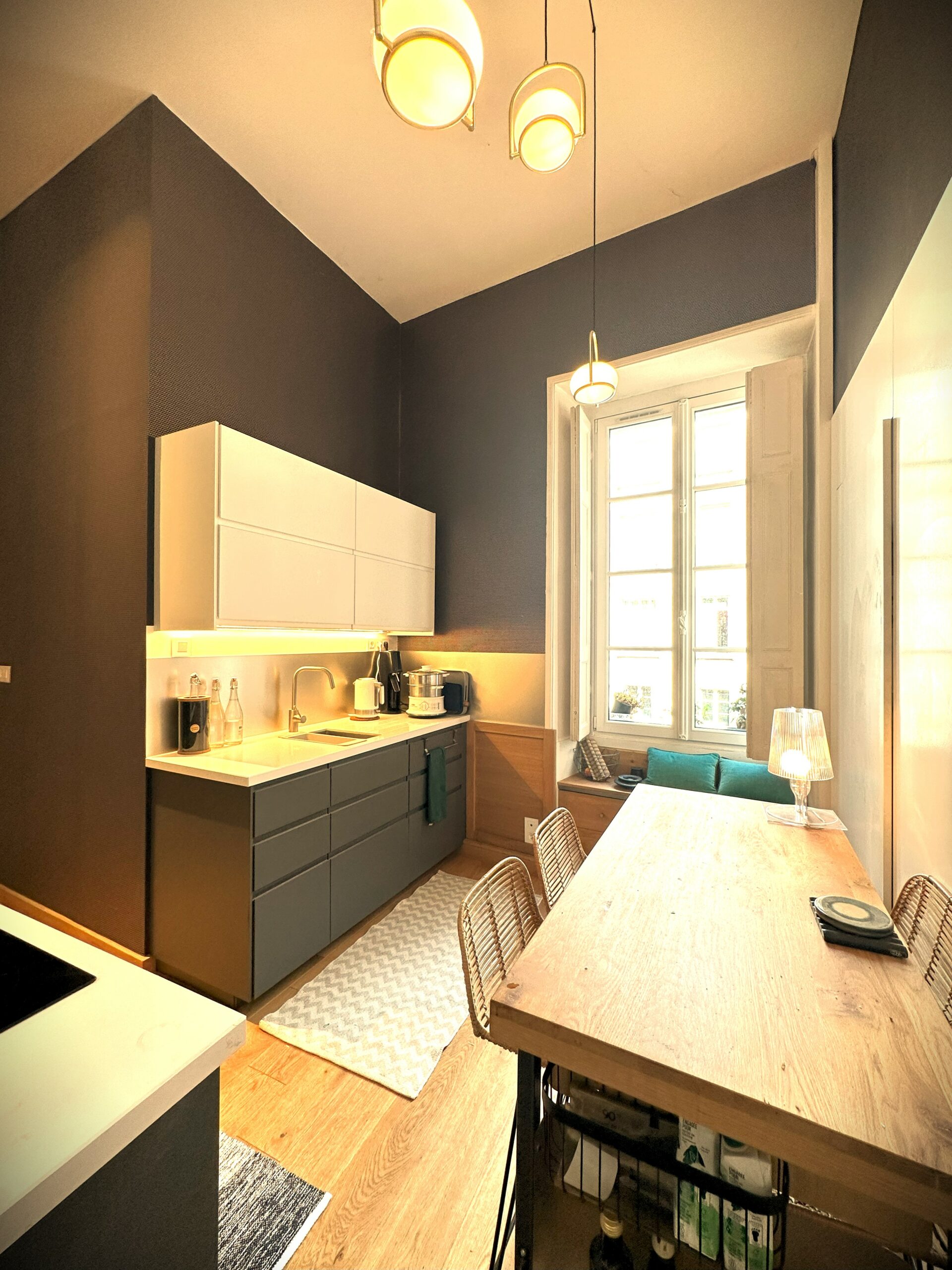 Cuisine moderne appartement, tons gris, sur parquet. Fenêtre lumineuse