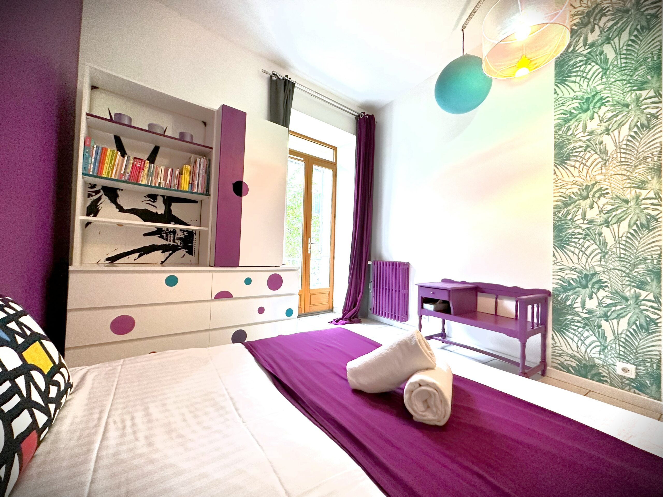Chambre avec lit fait, serviettes blanches et plaid visibles. Fenêtre donnant sur jardin