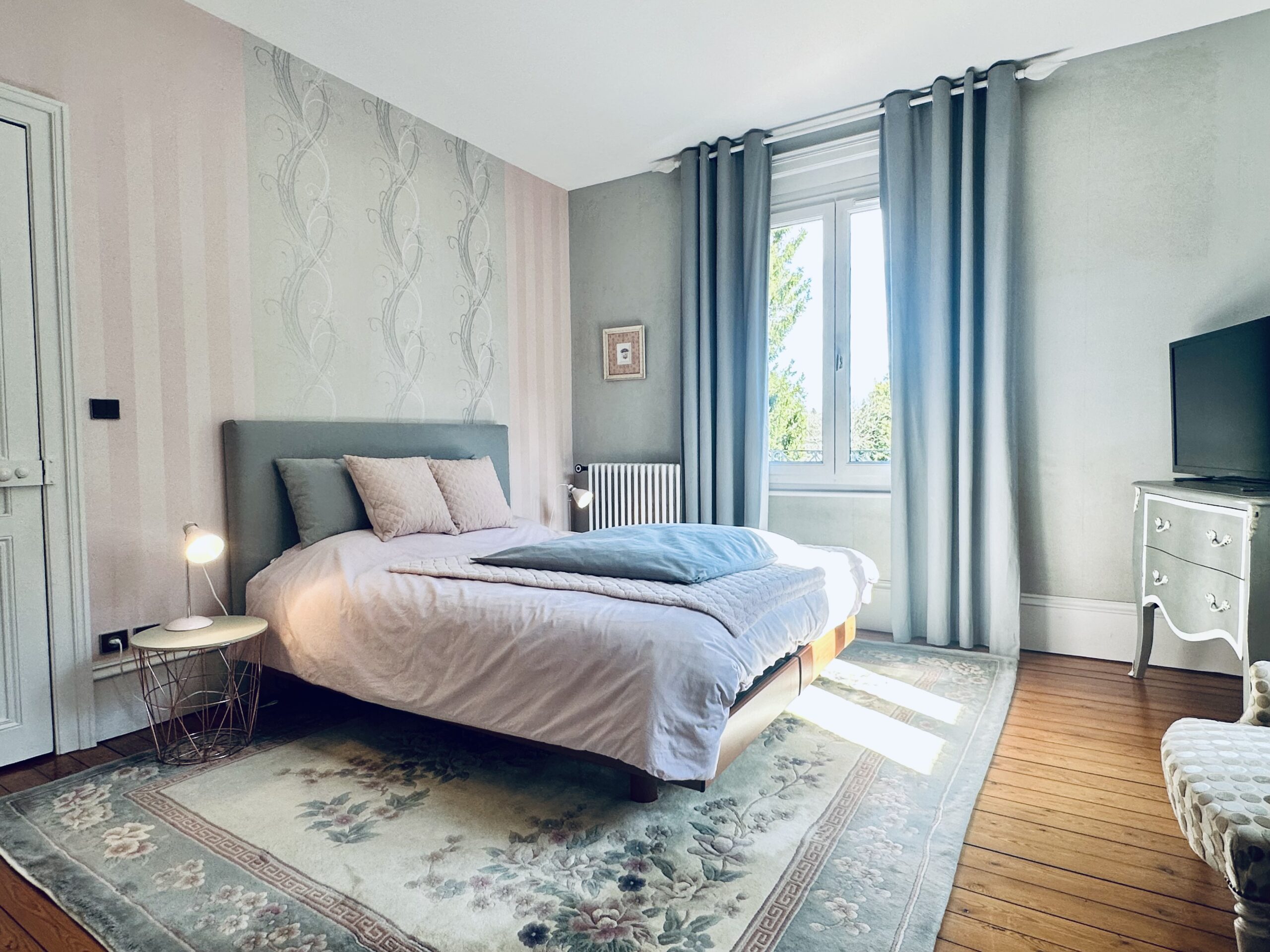 Grande chambre dans les tons bleu/vert et rose, sur parquet ancien, fenêtre donnant sur jardin
