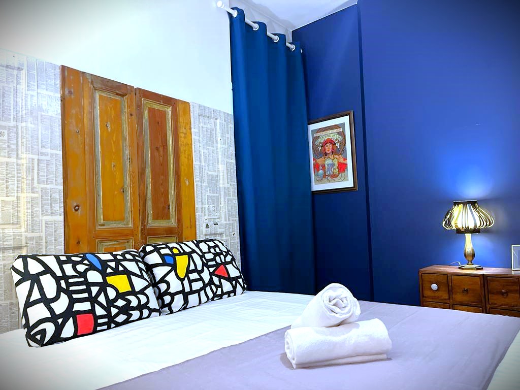Chambre avec lit fait, serviettes blanches sur le lit et murs bleu. Tête de lit en ancienne porte décorative