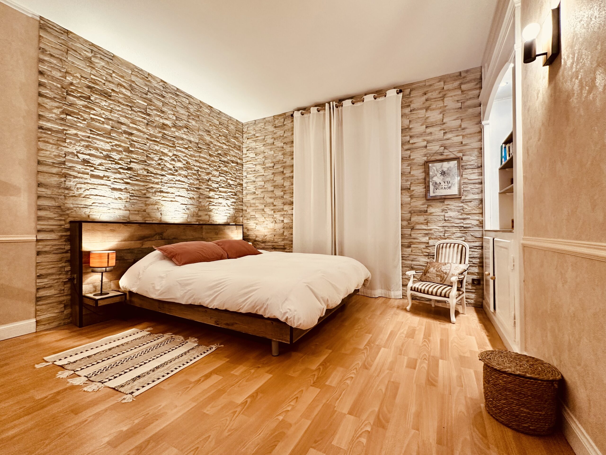 Grande chambre avec parquet, grand lit, deux murs avec briques de parement
