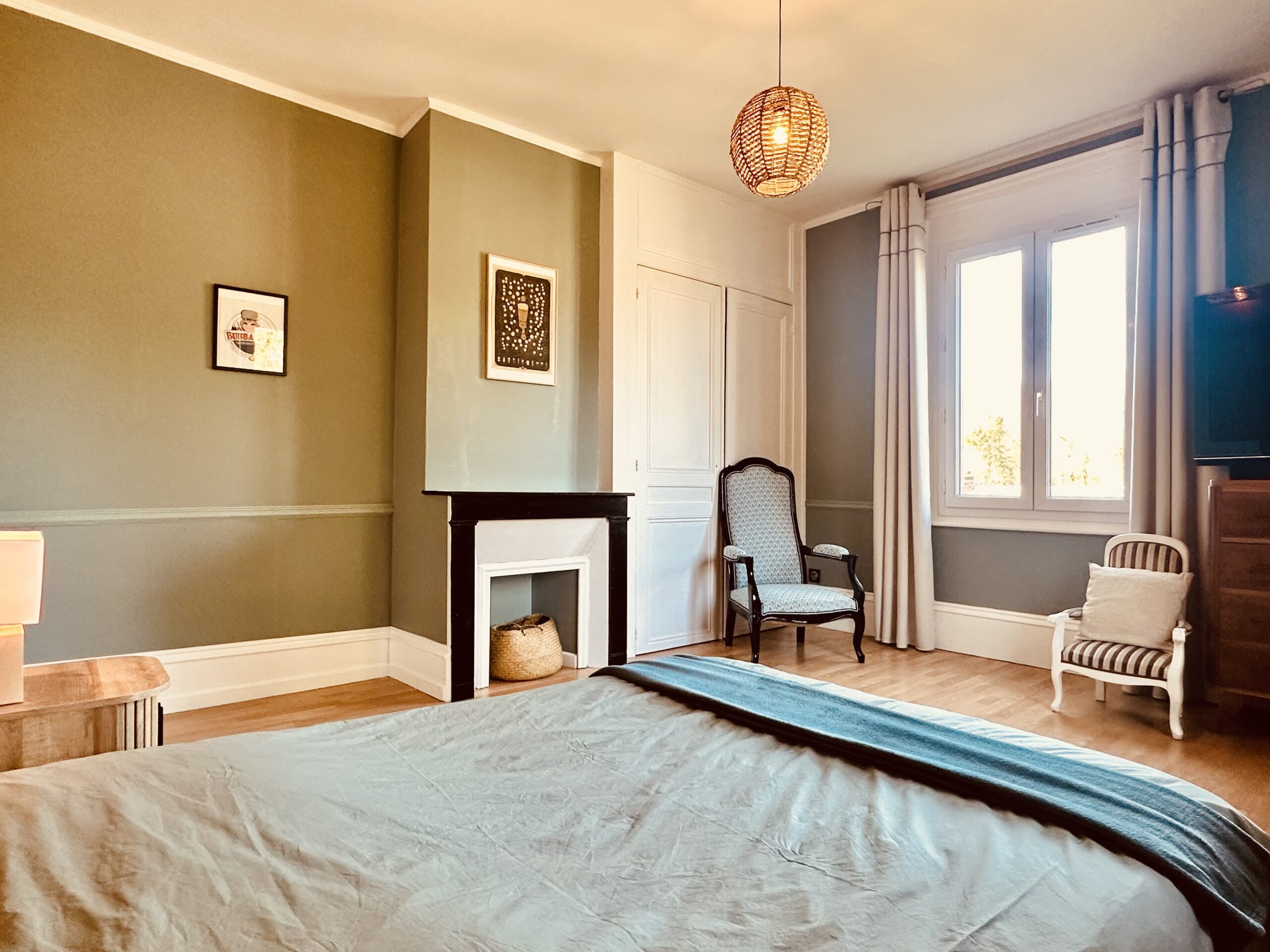 Grande chambre avec ancienne cheminée, murs vert et beige, sol en parquet